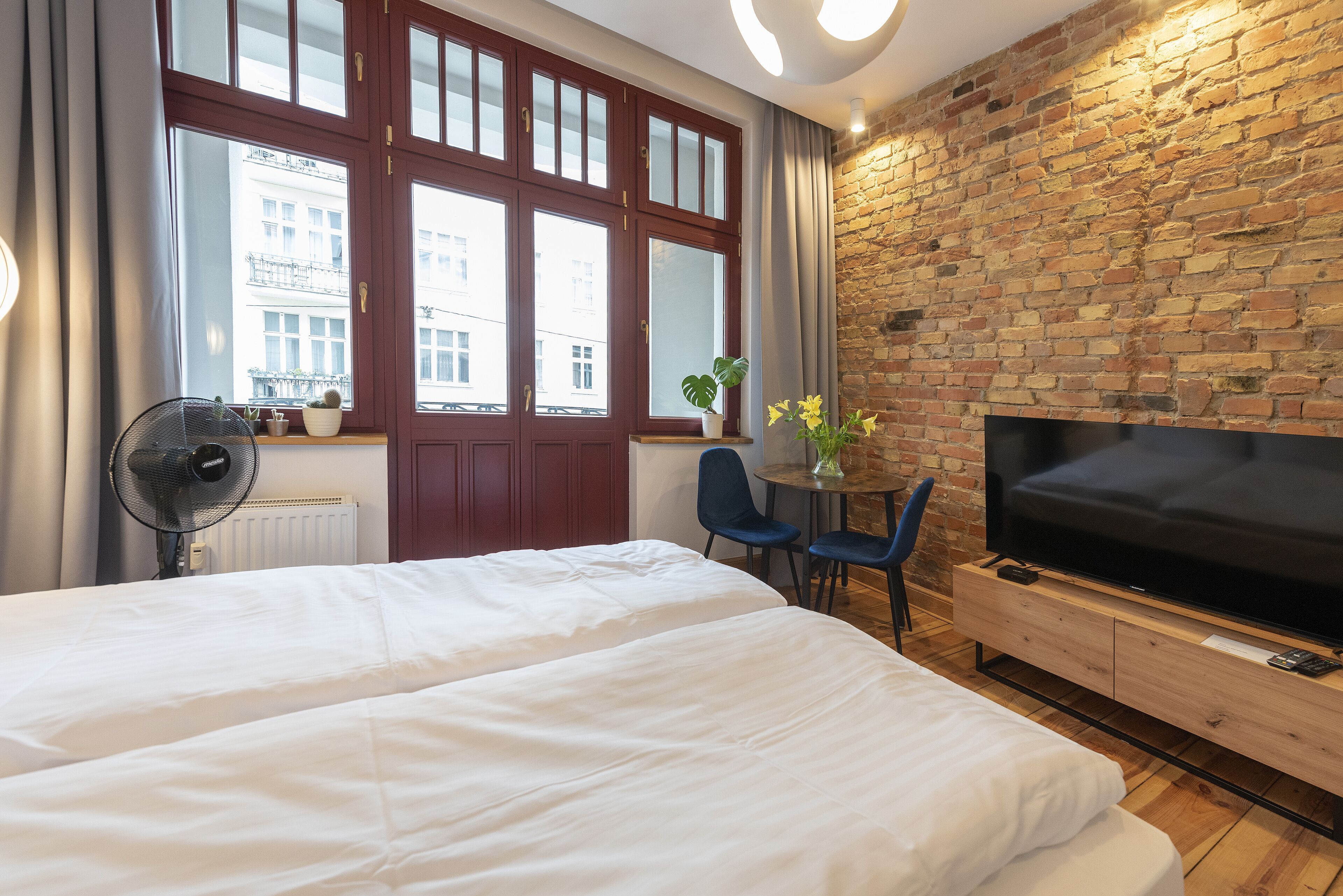 A hotel room with a large bed, a TV, a brick wall, and a window with curtains.