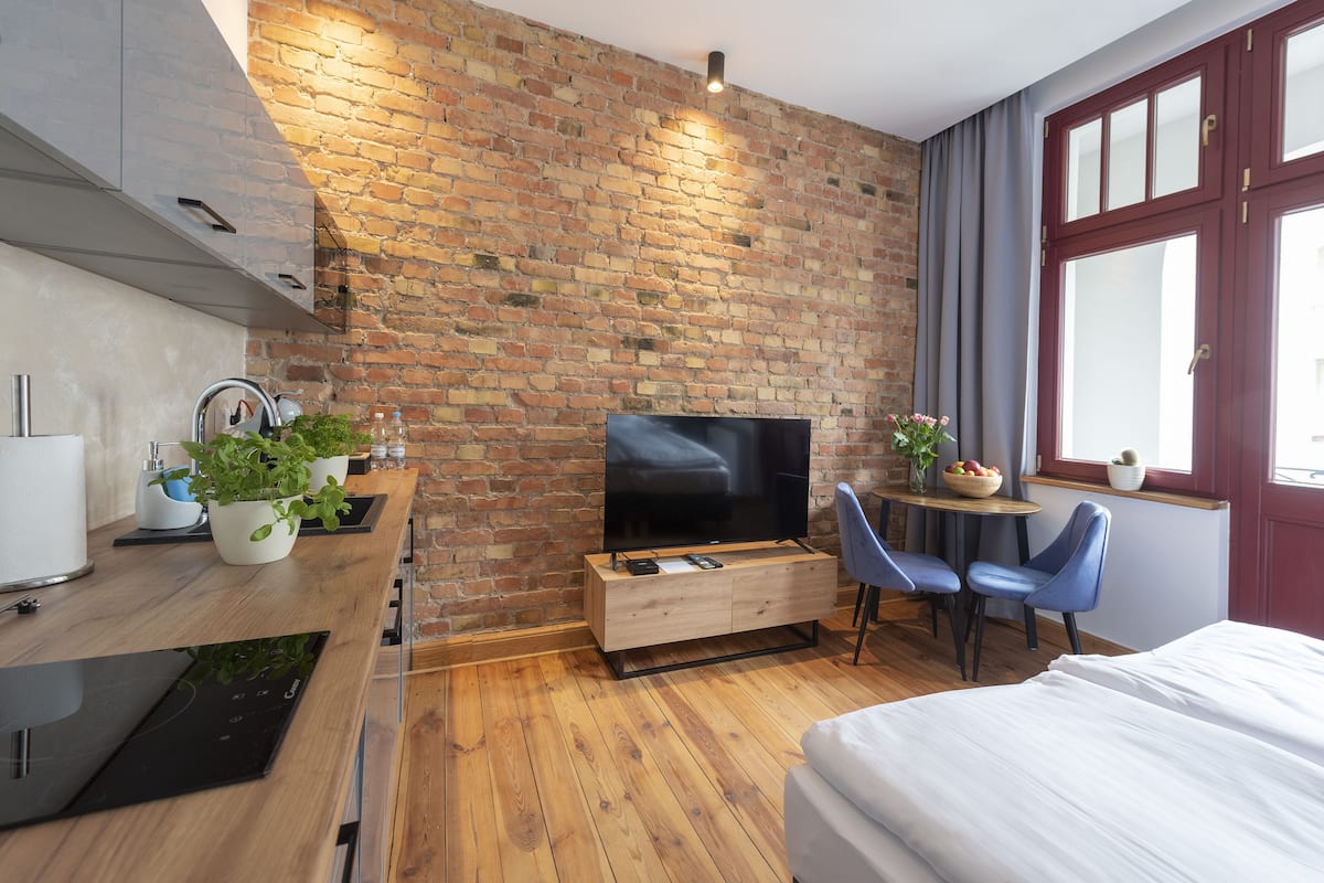 Une chambre moderne avec un mur en briques, un plancher en bois, un téléviseur à écran plat, un coin repas avec des chaises, une petite table et un lit.