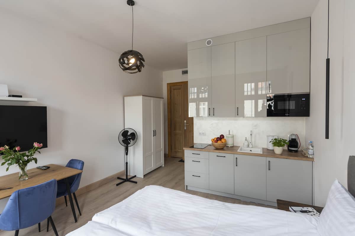 Ein modernes Hotelzimmer mit einem Bett, einem Schreibtisch mit Stuhl, einem Essbereich und einer Küchenzeile.