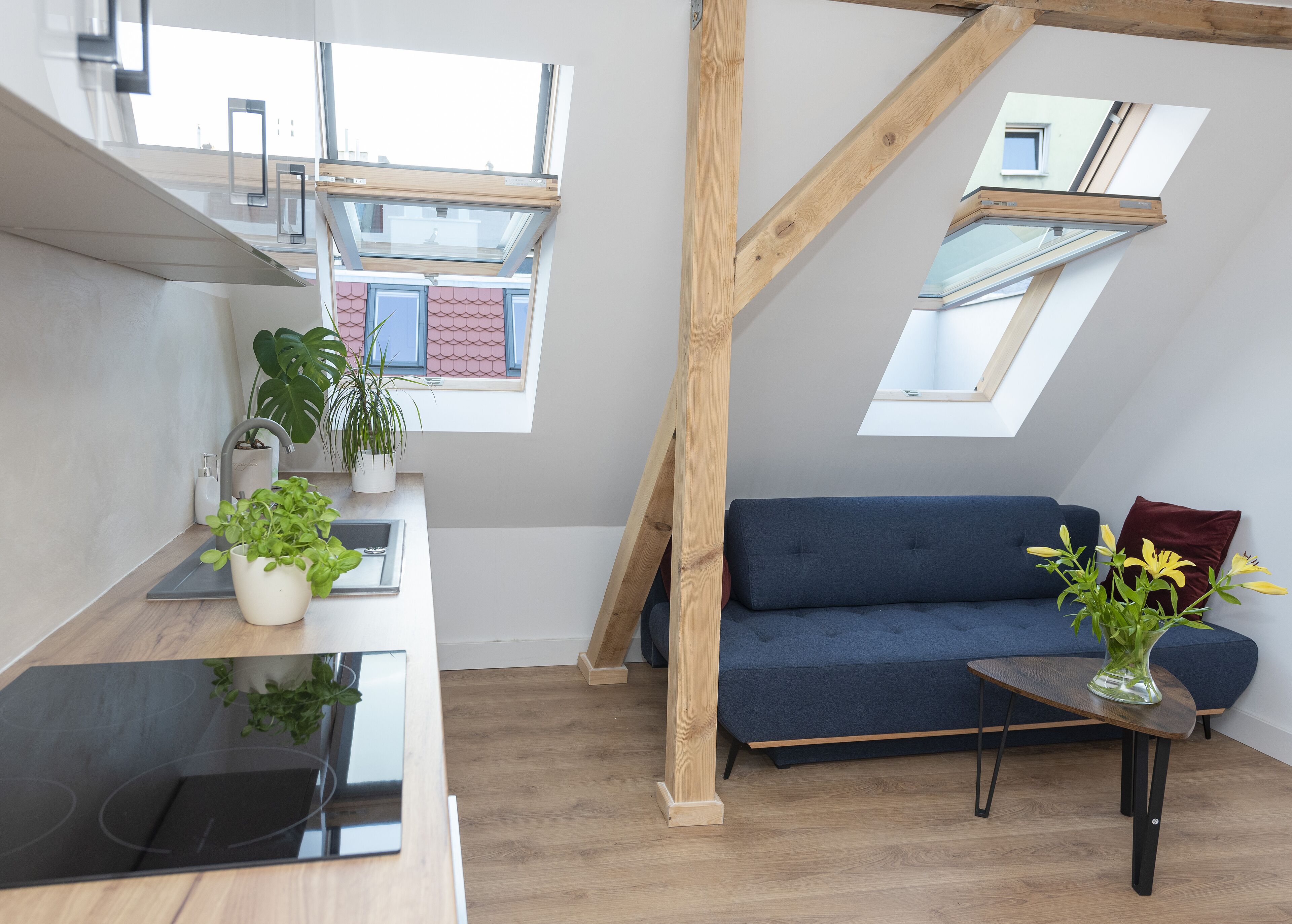 A modern loft apartment with a kitchen, a blue sofa, and skylights.