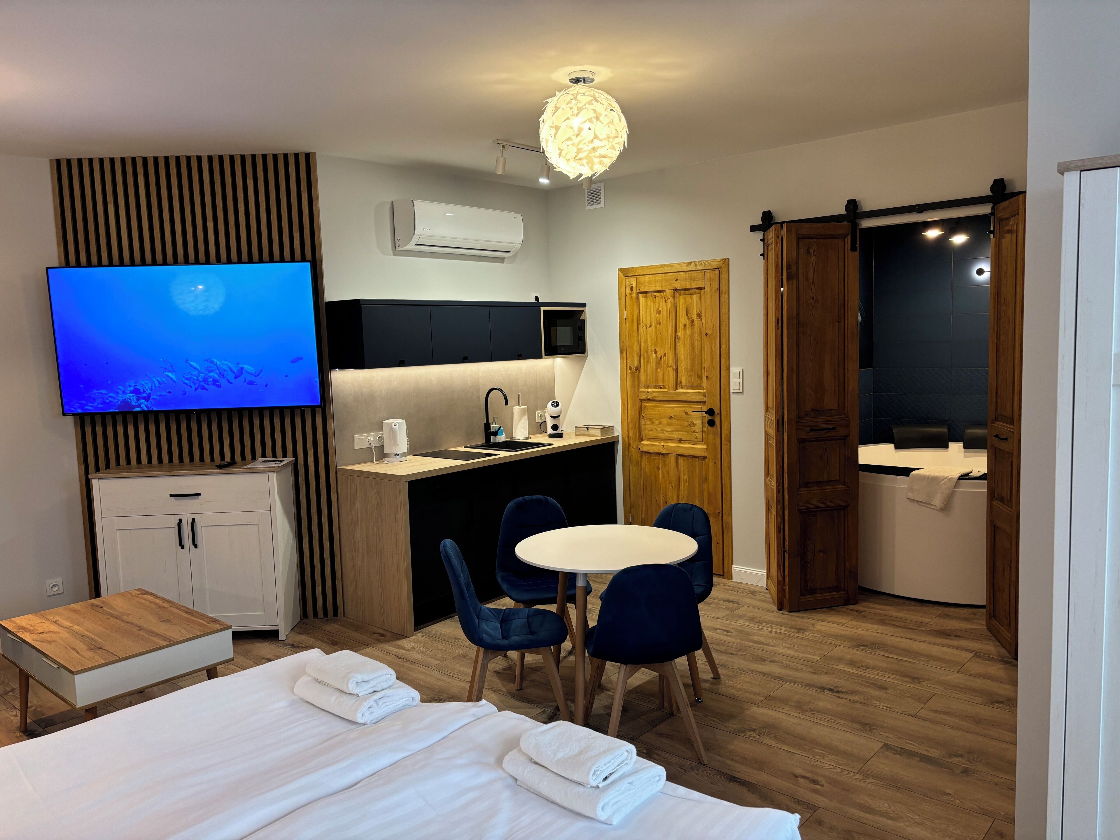 A modern hotel room with a bed, a desk, a TV, a shower, and a dining area.