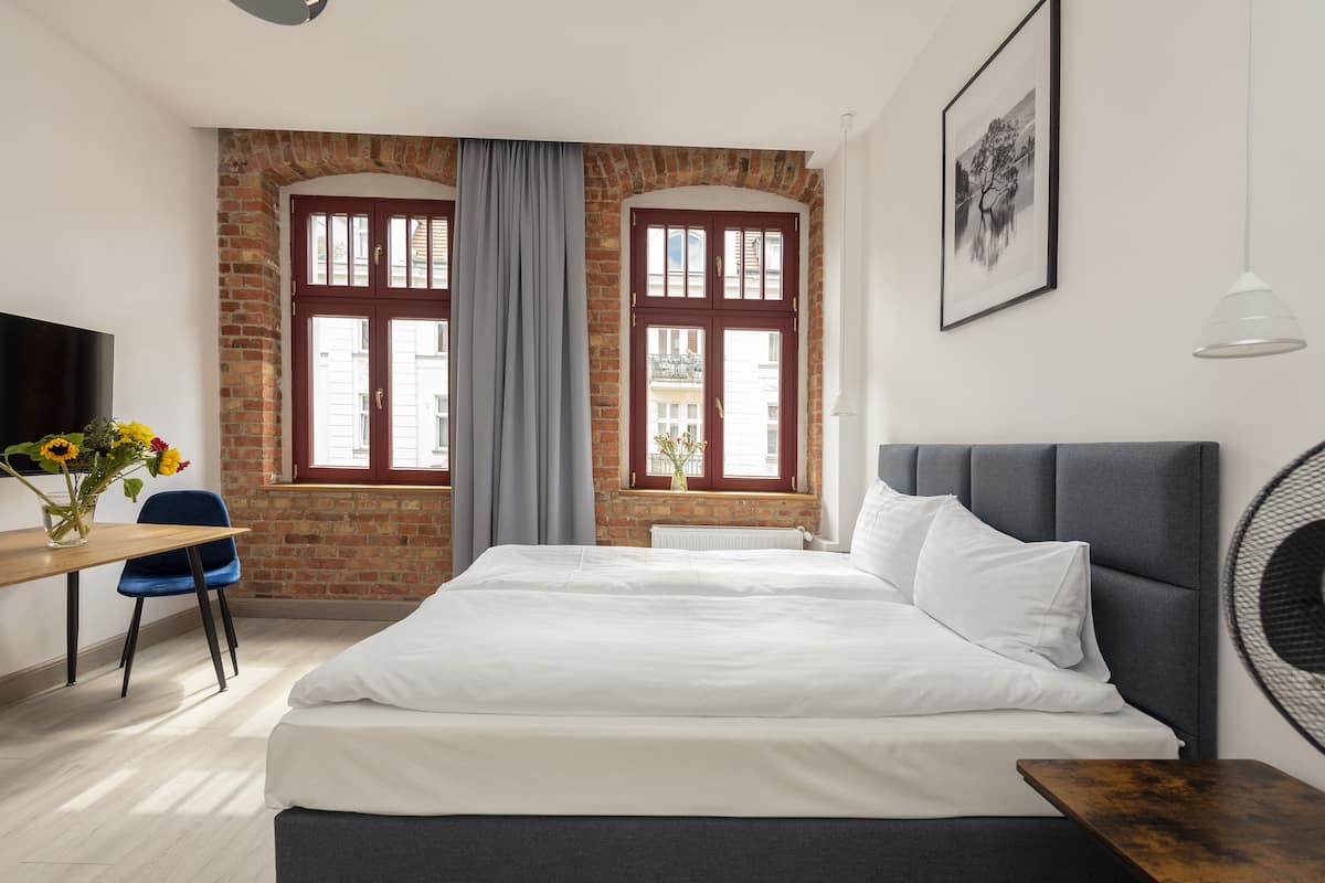 Une chambre à coucher avec un lit, un bureau, une chaise et une fenêtre avec des rideaux.