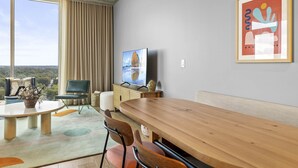 A modern room with a large window, a wooden dining table, and a television. - Luxe Rainey St High Rise | Heated Pool | Gym | ATX (Austin)