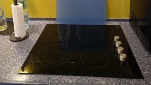 A kitchen with a black induction cooktop, yellow tiles, and a blue cutting board. - Aramis Colibri 72m2, lit King-size, Baignoire duo (Paris)