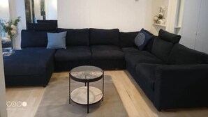 A modern living room with a sectional sofa, a glass coffee table, and a white wardrobe. - Aramis Colibri 72m2, lit King-size, Baignoire duo (Paris)