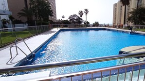 A swimming pool with a metal railing, surrounded by a fence, and palm trees in the background. - Appartement 90m2, Lumineux, Climatisé, Tout Confort, vue Mer, Toutes Commodités (Benalmádena)