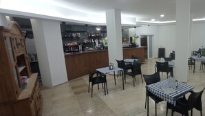 A spacious dining area with multiple tables and chairs, a bar area with shelves of bottles, and a view of the kitchen through an open doorway. - Appartement 90m2, Lumineux, Climatisé, Tout Confort, vue Mer, Toutes Commodités (Benalmádena)