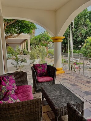 Un espacio de estar techado al aire libre con mobiliario de mimbre y vista a un jardín.