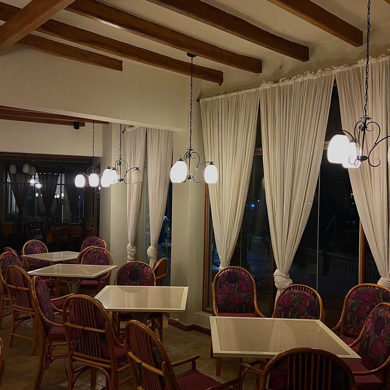 Interior de restaurante con vigas de madera, lámparas colgantes y mesas con sillas.