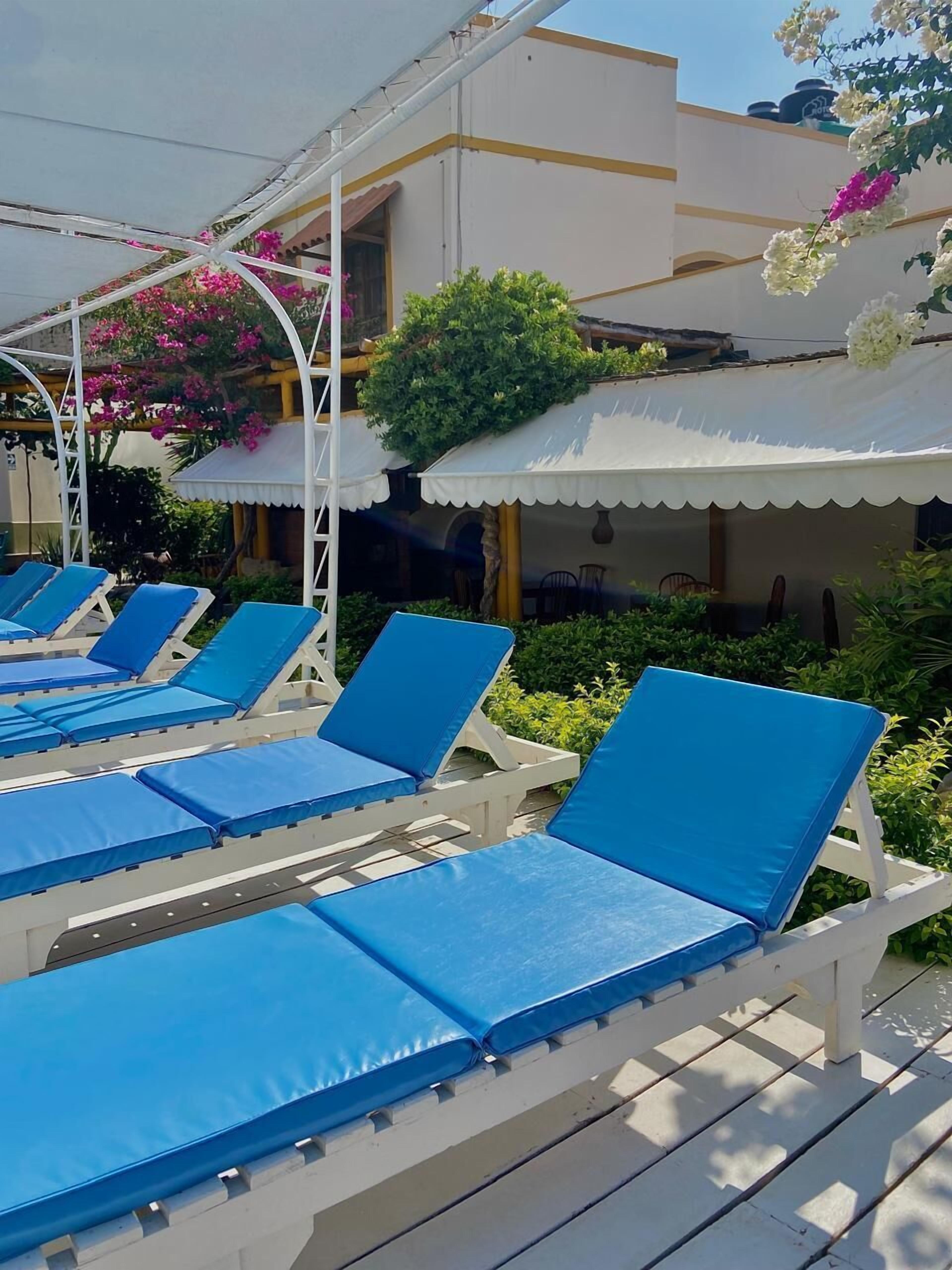 A row of blue lounge chairs with white frames, a white awning, and a building with yellow trim in the background.