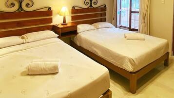 Habitación de hotel con dos camas individuales, una mesita de noche con lámpara y una ventana con cortinas.