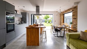 A modern kitchen with a central island, grey cabinetry, and a dining area with a green sofa and wooden table.