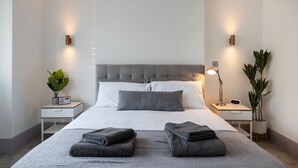 A modern hotel room with a large bed, two bedside tables, a nightstand, and a desk with a chair.