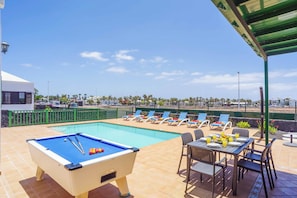 A pool area with a pool table, lounge chairs, and a dining table with plates and drinks. - Villa Brenas - Three Bedroom Villa, Sleeps 6 (Playa Blanca)