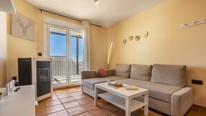 Un soggiorno con divano, tavolino e televisore. È presente un balcone con vista.