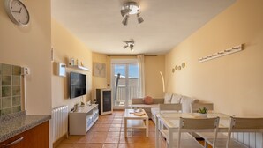 Una cucina moderna con forno integrato, un'area pranzo con tavolo e sedie, un divano e una TV fissata al muro.