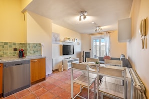 A compact kitchen with a dishwasher, a TV, and a dining area with a table and chairs.