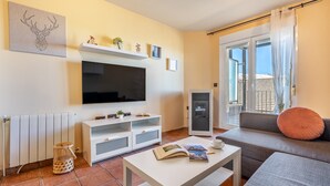 A living room with a TV, sofa, and a table with books. - Superior Apartment 31 C with Mountain Views, Private Terrace, and Wi-Fi (Sierra Nevada)