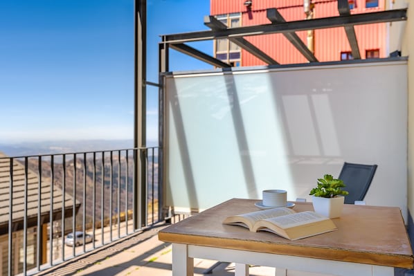 A balcony with a table, a potted plant, and an open book.