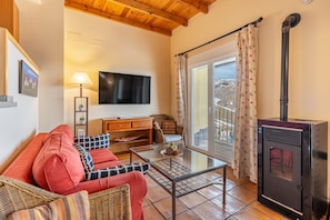 A cozy living room with a sofa, a glass coffee table, a TV, a fireplace, and a view of the outdoors.