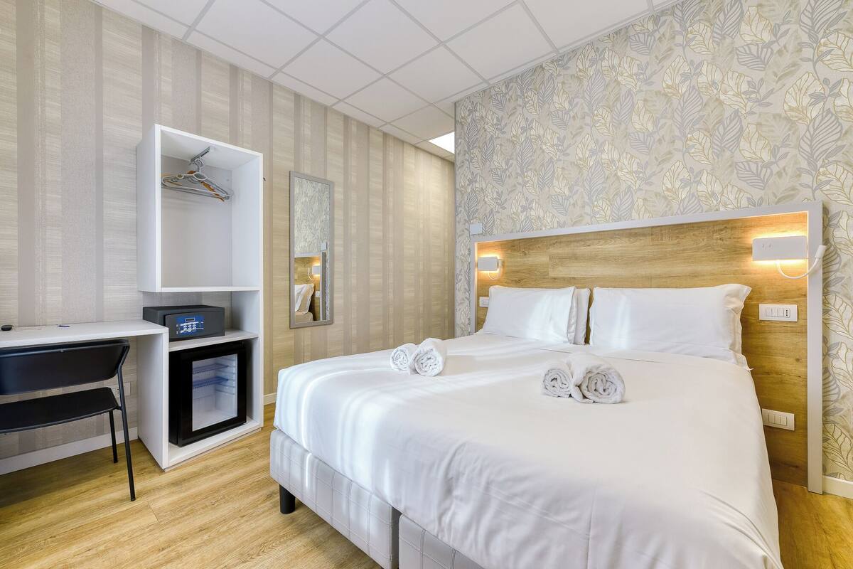 A hotel room with a bed, a desk, and a wardrobe.