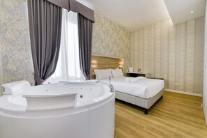 Una habitación de hotel moderna con una bañera grande, dos camas, un cabecero de madera y una mesita de noche con lámpara.