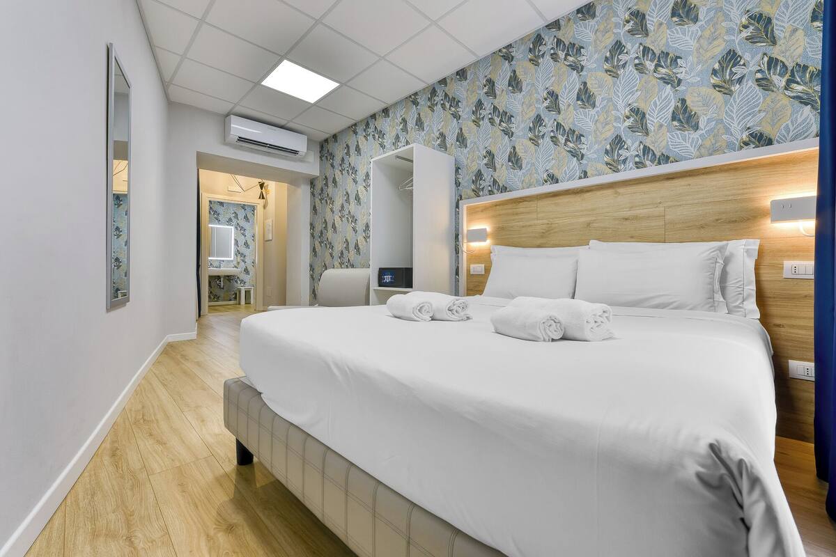 A hotel room with a large bed, a wooden headboard, and a floral wallpaper design.