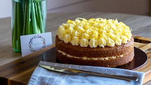 Un gâteau recouvert d’un glaçage jaune et un vase rempli de fleurs jaunes, le tout posé sur une table en bois.