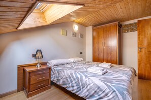A bedroom with a sloped ceiling, a bed with a patterned bedspread, a bedside lamp, a wooden dresser, and a wardrobe. - Holiday Apartment "Duplex 23 E" with Mountain Views, Private Terrace and Wi-Fi (Monachil)
