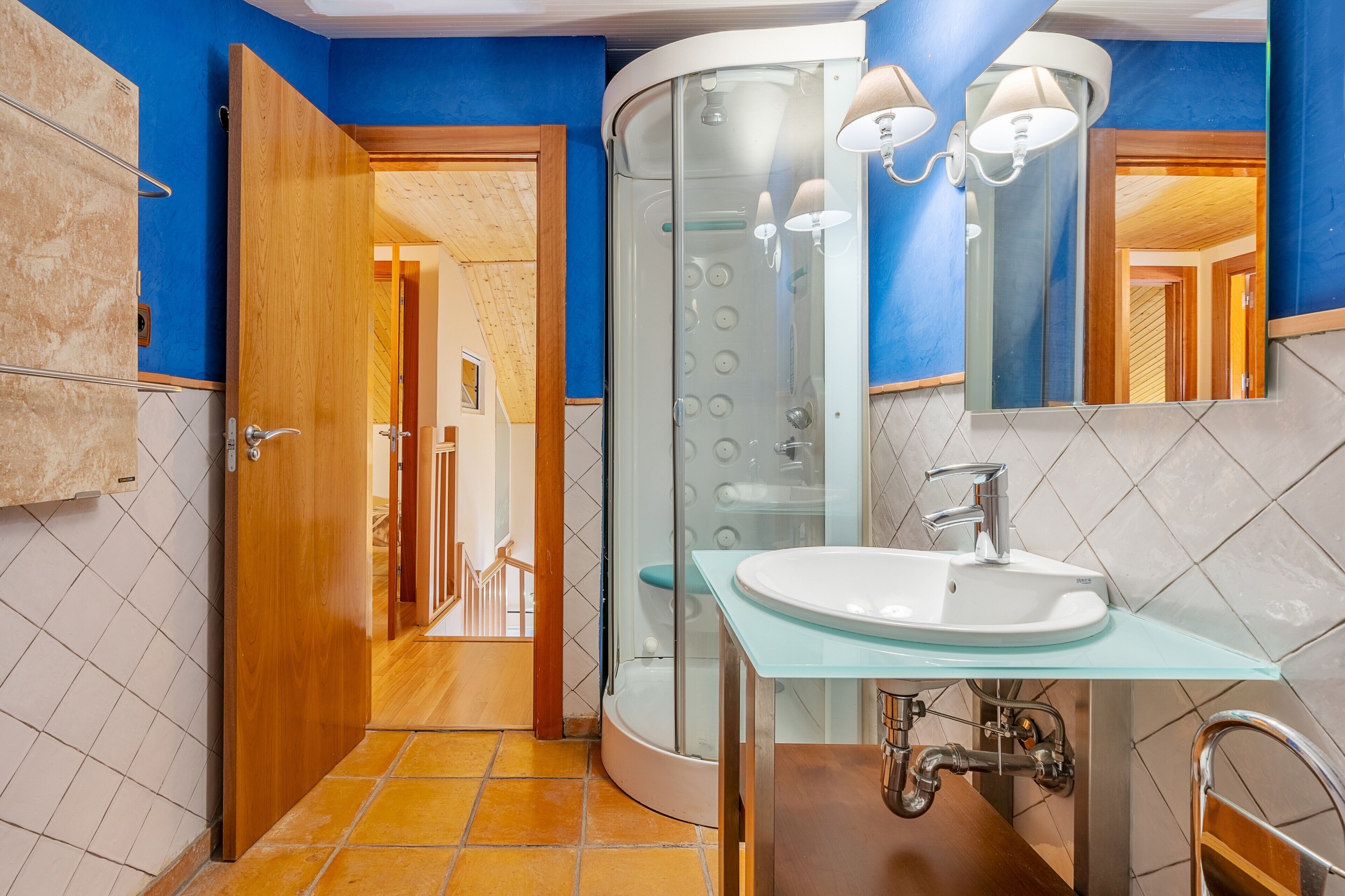A bathroom with a glass shower enclosure, a white sink, and a wooden door.