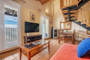 A living room with a TV, wooden furniture, a balcony, and a staircase.