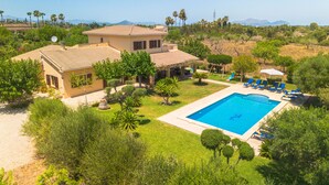 Ein zweigeschossiges Haus mit Swimmingpool, umgeben von viel Grün und Palmen.
