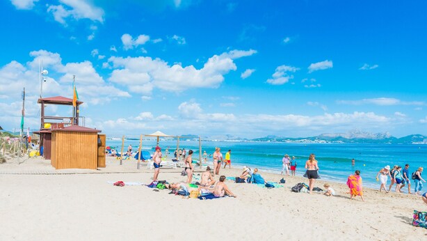 Ein Strand mit einem Rettungsturm, Sonnenschirmen und Menschen, die Sonnenbaden.