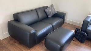 Ein schwarzes Ledersofa mit passendem Hocker und einem Kissen mit Muster auf Holzdielen.