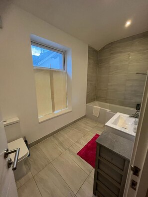 Huis | Badkamer | Een bad/douchecombinatie, een diep bad, een haardroger, handdoeken