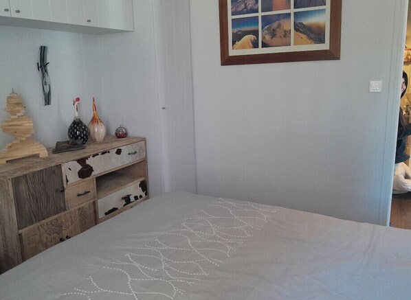 A bedroom with a bed, a dresser with decorative items, a framed picture on the wall, and a window with a view.