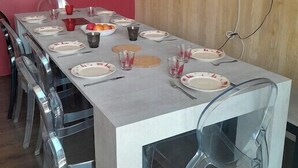 A modern dining area with a long table set for six, clear plastic chairs, and artwork on the walls. - Ski in and ski out apartment Superdévoluy (Le Dévoluy)