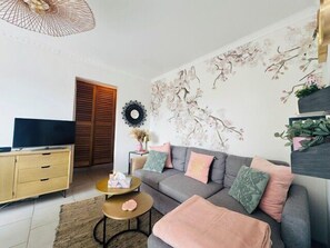 Una sala de estar con sofá, mesa de centro, televisor y decoración en la pared.