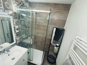 Ein Badezimmer mit Duschkabine aus Glas, einem weißen Waschbecken und einer gefliesten Wand.