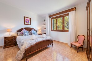 A neatly arranged bedroom with a wooden bed, bedside tables, a chair, a window with curtains, and a shelf unit.