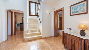 A spacious hallway with a staircase, a wooden cabinet with a lamp, and a framed picture on the wall. - Rental Villa Manresa in Alcudia by JS Villas (Alcudia)
