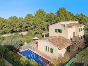 A two-story building with a swimming pool, surrounded by greenery and trees.