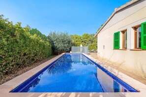 A rectangular swimming pool with a clear blue water surface, surrounded by a low stone wall and lush greenery.