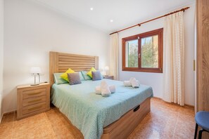 A bedroom with a wooden headboard, a bed with a green patterned bedspread, two bedside lamps, and a window with curtains.