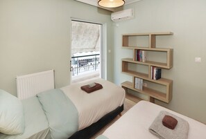 A bedroom with two beds, a window with a view, a bookshelf, and an air conditioning unit.