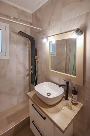 A modern bathroom with a white sink, a handheld showerhead, and a mirror with lights.