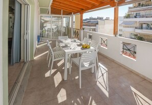 A balcony with a dining table set for four, white chairs, and a fruit bowl.