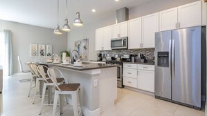 Una cocina moderna con armarios blancos, electrodomésticos de acero inoxidable e iluminación colgante.