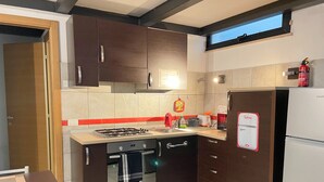 A modern kitchen with dark cabinets, a gas stove, a built-in oven, a refrigerator, and a window above the sink.