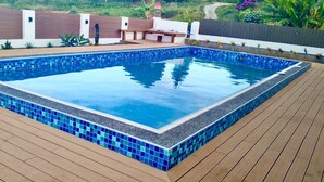 Ein rechteckiger Swimmingpool mit blauen Mosaikfliesen, umgeben von einer Holzterrasse.